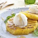 grilled pineapple with ice cream on top and mint leaves and syrup
