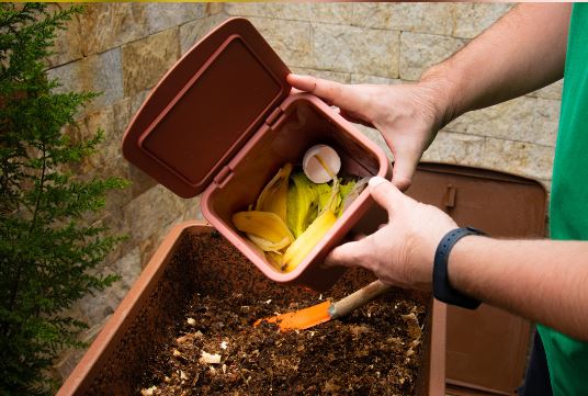 Hands placing kitchen vegetable scraps into a compost bin