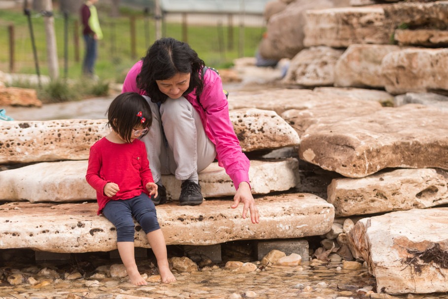 A woman and her daughter cooling off at the No Name Creek water feature at San Antonio Botanical Garden