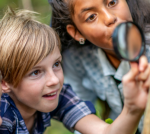 Two youngsters exploring the outdoors with a magnifying glass